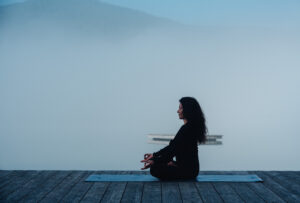 Frau in Meditation auf einer Yogamatte an einem stillen, nebligen Bergsee